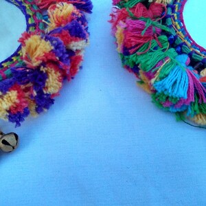 May include: Two round mirrors with colorful yarn fringe and small bells hanging from the bottom. The mirrors are surrounded by a woven design with a variety of colors, including purple, pink, yellow, green, and blue.