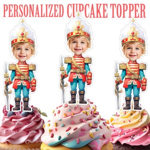 以下が含まれることがあります： 漫画の兵士のデザインが施された、パーソナライズされたカップケーキトッパーが3つ。トッパーは、カラフルなフロスティングとスプリンクルが施されたカップケーキの上に配置されています。兵士は笑顔で、金色のアクセントが付いた白い帽子、赤と青の制服を着ています。「PERSONALIZED CUPCAKE TOPPER」の文字が上部にあります。