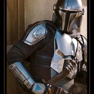 May include: A full-body suit of metallic armor featuring a polished silver helmet with a T-shaped visor, a chest plate, shoulder pauldrons with a skull emblem, and gauntlets. The armor is worn over a dark fabric undersuit with a utility belt and bandolier.