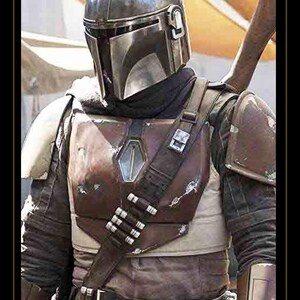 May include: A metallic silver helmet with a T-shaped visor worn over a dark brown chest plate featuring a central emblem, a diagonal bandolier with silver cartridges, shoulder pauldrons, and a dark fabric under-suit with a utility belt.
