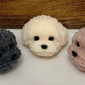 May include: Three dog-shaped candles, one black, one white, and one pink. The candles are all in the shape of a poodle.