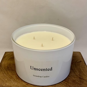 May include: A white, three-wick candle in a glass jar with a label that reads "Unscented" and "Snowdrop Candles".