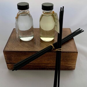 May include: Two glass bottles with black lids filled with clear liquid, sitting on a wooden box with black diffuser sticks.