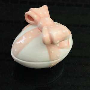 May include: A white ceramic egg-shaped trinket box with a pink polka dot ribbon and bow.