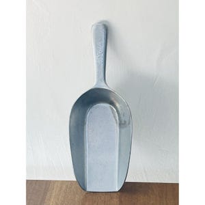 Peut inclure: Une pelle en métal argenté avec un long manche et un large bol ovale. Le manche porte le texte "#XSA". La pelle est conçue pour prélever des produits secs.