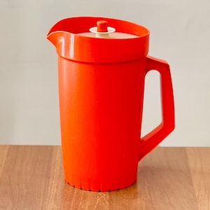 Op de afbeelding: Een felrode plastic kan met bijpassende deksel en handvat. De kan heeft een klassiek ontwerp, ideaal voor het serveren van drankjes. De kan is gemaakt van duurzaam plastic en is geschikt voor zowel binnen als buiten.