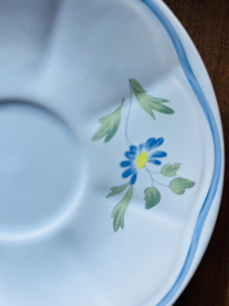 May include: A light blue saucer with a scalloped edge and a blue and green floral design. The flower has a yellow center.