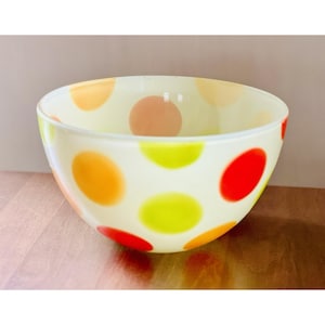 Può includere: Una ciotola rotonda in vetro bianco sporco con pois colorati rossi, arancioni e gialli. La ciotola ha una finitura liscia e lucida ed è probabilmente utilizzata per servire cibo o come elemento decorativo.