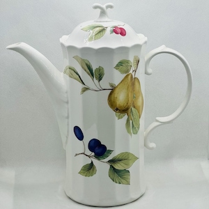 Pode incluir: Cafeteira de cerâmica branca com tampa, bico e alça. A cafeteira é decorada com um desenho de frutas e folhas com peras, ameixas e cerejas. A cafeteira tem uma textura canelada e um adorno decorativo na tampa.