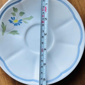 May include: A light blue ceramic saucer with a blue and yellow flower design and a blue rim. The saucer is 5.5 inches in diameter.