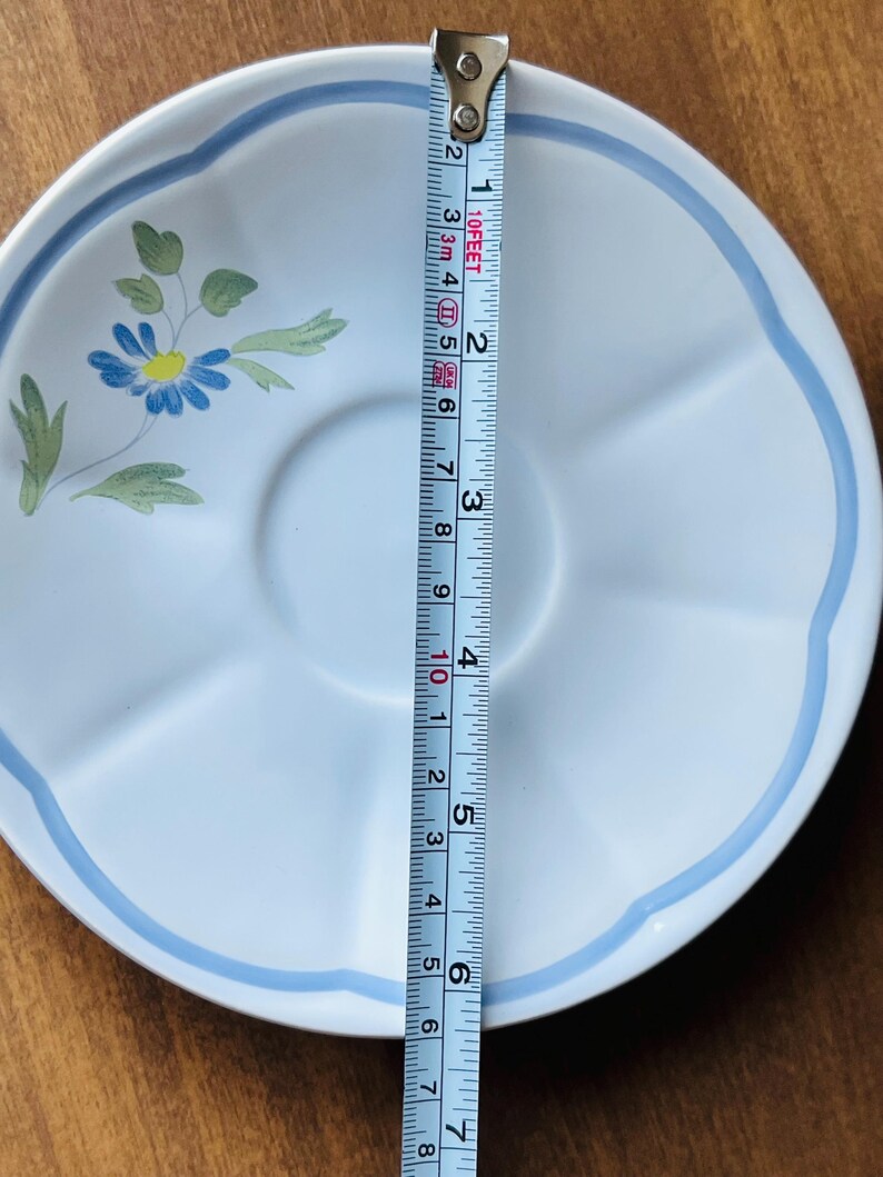 May include: A light blue ceramic saucer with a blue and yellow flower design and a blue rim. The saucer is 5.5 inches in diameter.