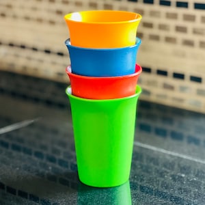 May include: A stack of four colorful plastic cups. The cups are in shades of green, red, blue, and orange. The cups are stacked on top of each other, with the green cup at the bottom and the orange cup at the top.