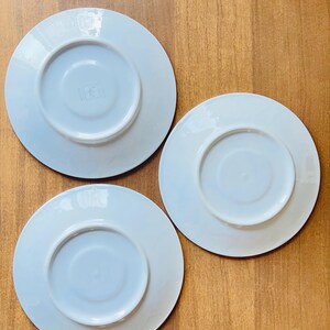 May include: Three white ceramic saucers with a slightly raised rim. The saucers are all the same size and shape.