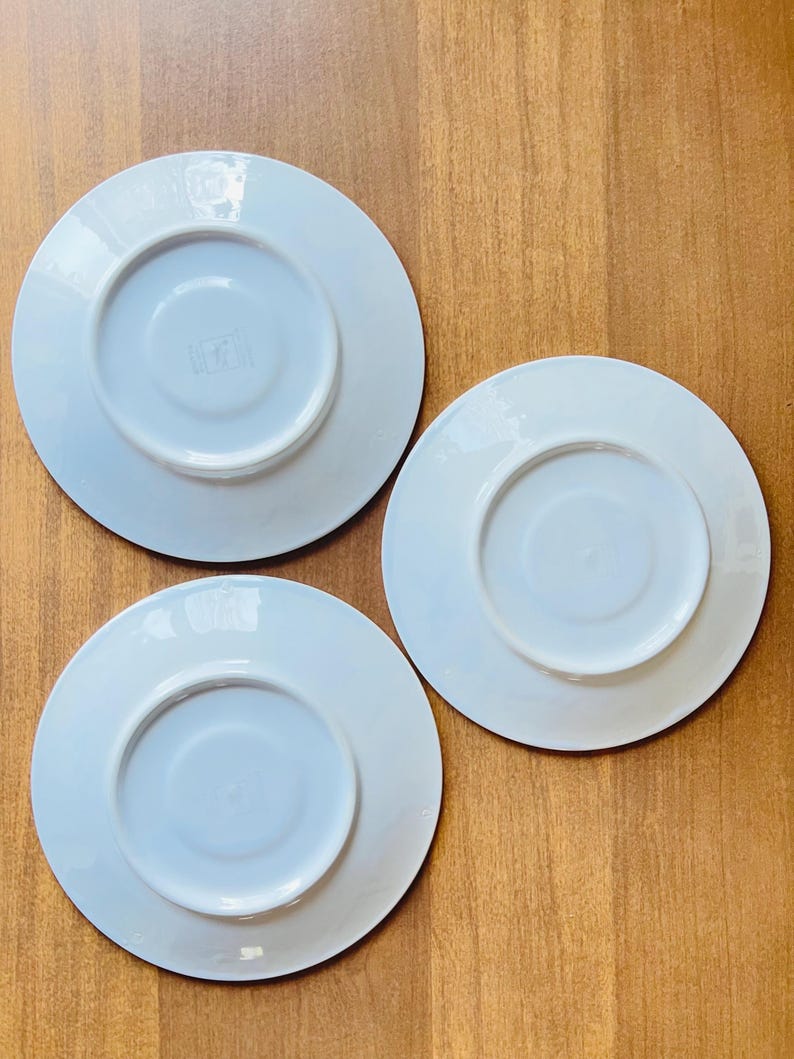 May include: Three white ceramic saucers with a slightly raised rim. The saucers are all the same size and shape.