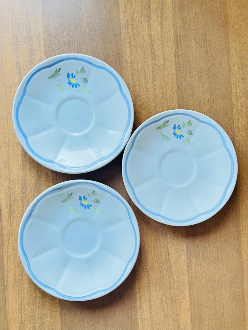 May include: Three white ceramic saucers with a blue rim and a blue flower design.
