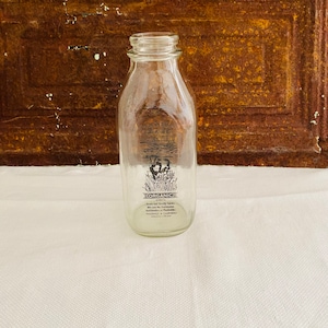 May include: A clear glass milk bottle with a black and white label that reads "ORGANIC" and "From our family farms. We use no hormones. Antiobiotics or Pesticides.  PASADENA, CALIFORNIA".
