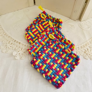 May include: Set of four woven pot holders in yellow, blue, pink, and purple. The pot holders are made of a woven fabric and have a square shape.