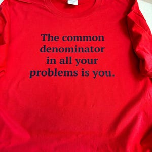 May include: Red t-shirt with black text that reads "The common denominator in all your problems is you."
