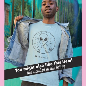 K&ouml;nnte beinhalten: Ein hellblaues T-Shirt mit einer schwarzen und wei&szlig;en Grafik eines Au&szlig;erirdischen mit dem Text "STAY QUEER" darunter.