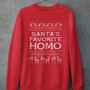K&ouml;nnte beinhalten: Roter Weihnachtspullover mit einem wei&szlig;en pixelartigen Design von Rentieren und dem Text "SANTA'S FAVORITE HOMO".