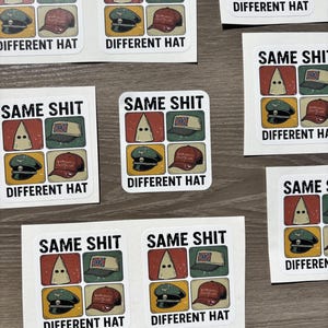 Peut inclure: Feuilles d'autocollants blancs avec le texte "SAME SHIT" au-dessus d'un graphique d'une cagoule du KKK et de trois chapeaux différents. Le texte "DIFFERENT HAT" est en dessous des chapeaux. Les autocollants sont sur une surface brun clair.