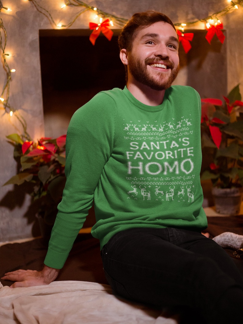 K&ouml;nnte beinhalten: Ein gr&uuml;ner Weihnachtspullover mit einem wei&szlig;en Design, das "Santas Lieblings-Homo" sagt.