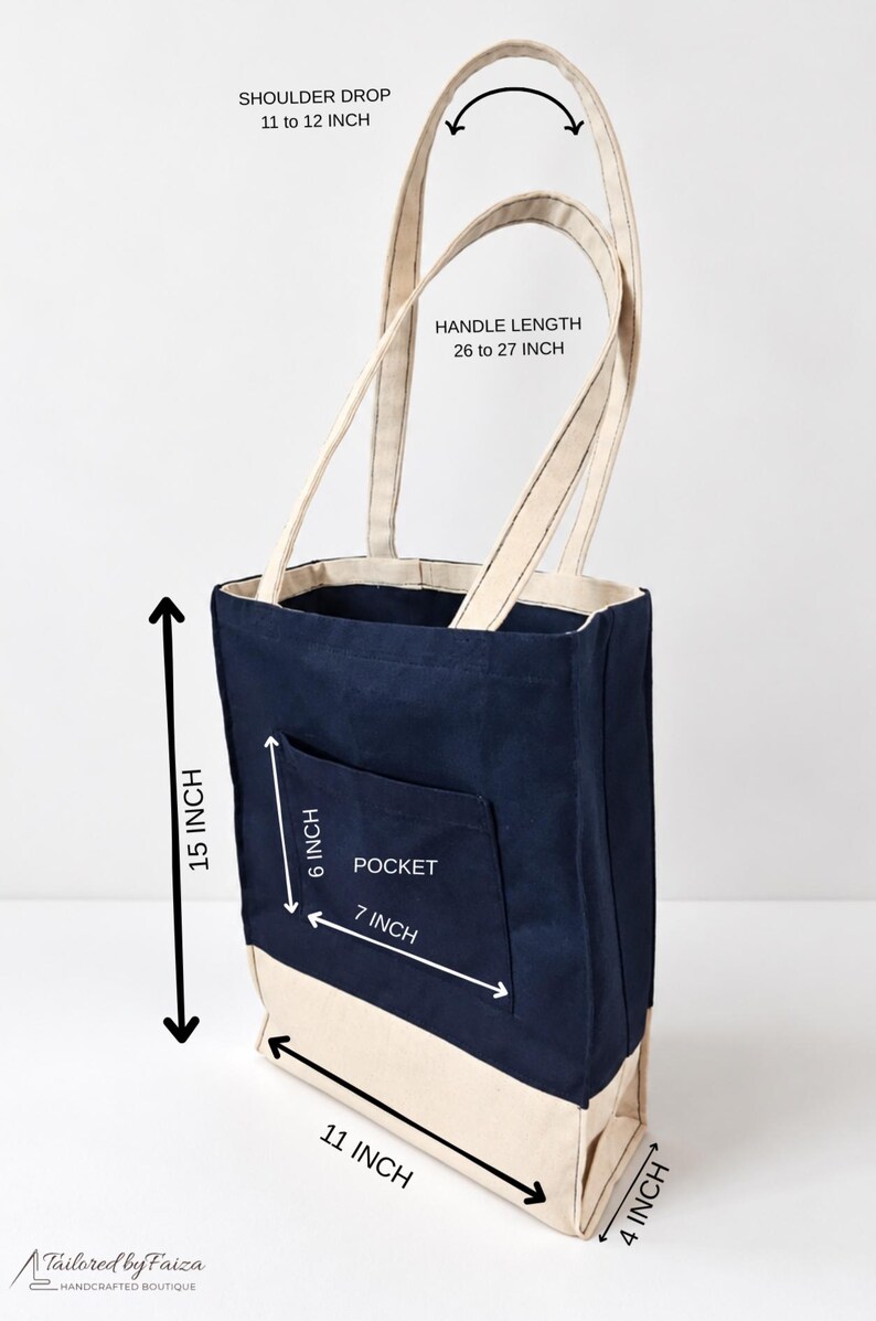 Puede incluir: Un bolso tote de lona azul marino y beige con un bolsillo frontal. Las dimensiones son 38,1 cm de alto, 27,9 cm de ancho y 10,2 cm de profundidad. Tiene asas de 66 a 68,6 cm. El texto dice Tailored by Faiza.