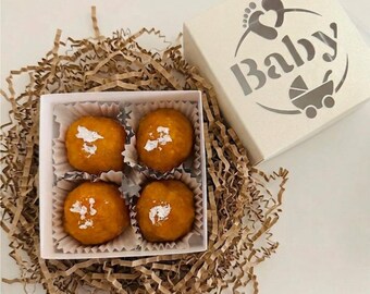 Puede incluir: Una caja blanca con la palabra "Baby" y un gráfico de cochecito, junto a una caja de cuatro dulces mithai naranjas. Los dulces están en una caja blanca, metidos en papel marrón. El texto "Mithai & Treat Boxes" está en la parte superior.
