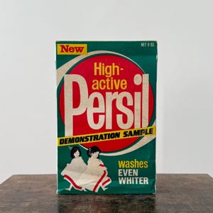 May include: Vintage Persil laundry detergent box. The box is green with a red circle in the center, featuring the brand name and the words "High-active". The box also says "Demonstration Sample" and "Washes Even Whiter". The box is labeled "New" and "Net 255 g."