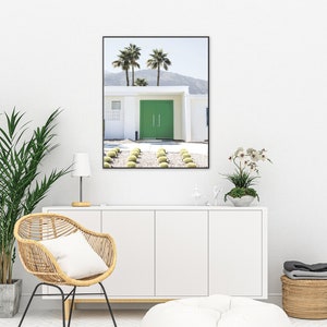 May include: A framed photograph of a modern, white house with a bright green door. The house is surrounded by palm trees and a gravel driveway.