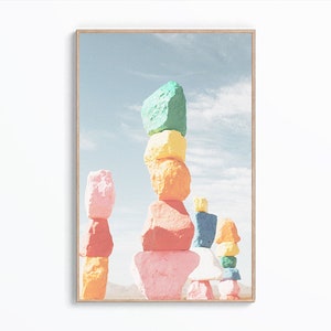 Puede incluir: Una pila de rocas coloridas pintadas en tonos de rosa, verde, amarillo, naranja y azul. Las rocas están apiladas unas sobre otras de una manera caprichosa y abstracta.