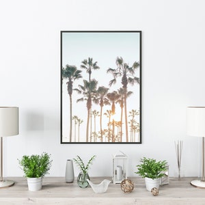 May include: A framed photograph of a row of palm trees against a light blue sky. The photo is displayed on a wooden shelf with two white lamps, two potted plants, a vase, a lantern, and a decorative bird sculpture.