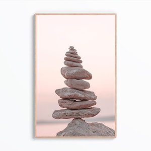 May include: A stack of grey stones balanced on top of each other in a pyramid shape against a pink and white sunset background.