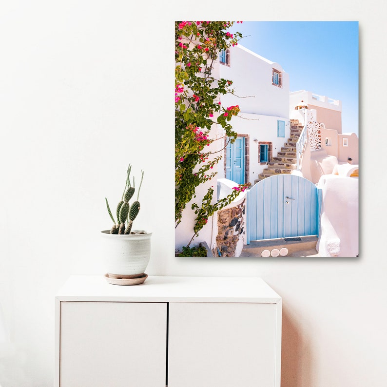 Puede incluir: Un edificio blanco con una puerta azul y una escalera de piedra. Flores rosas crecen en una vid a lo largo del lado del edificio.