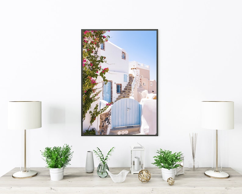 Puede incluir: Una fotograf&iacute;a enmarcada de un edificio blanco con una puerta azul y una enredadera trepadora con flores rosas. El edificio est&aacute; en un lugar soleado con un cielo azul.