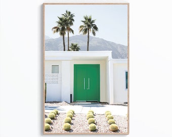 Op de afbeelding: Een wit modern huis uit het midden van de eeuw met een felgroene dubbele deur. Palmbomen en cactussen staan in de voortuin.