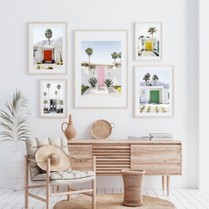 May include: Five framed photographs of mid-century modern homes with colorful front doors. The photos are hung on a white wall above a light wood dresser and a wicker chair.