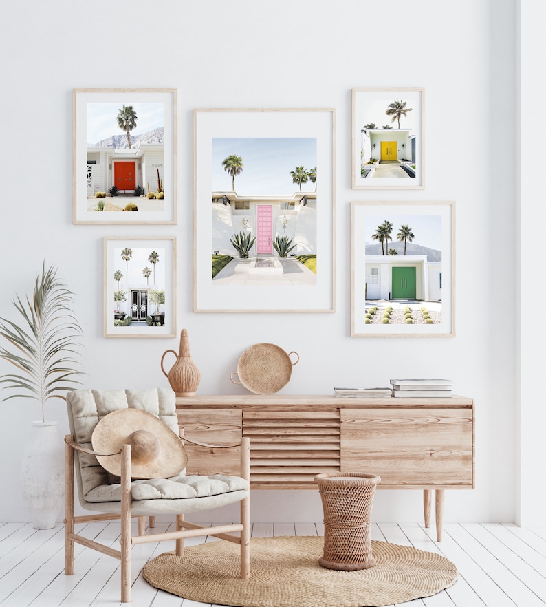 May include: Five framed photographs of mid-century modern homes with colorful front doors. The photos are hung on a white wall above a light wood dresser and a wicker chair.