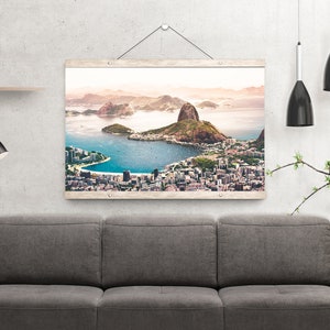 May include: A framed photograph of a city skyline with a large mountain in the background. The city is located on a peninsula with a body of water surrounding it. The photograph is in a wooden frame with a white background.