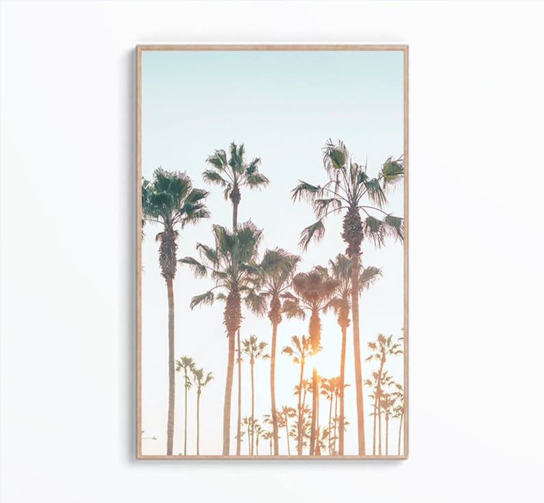 May include: A framed print of a photograph of a row of palm trees silhouetted against a blue sky with a bright orange sunset in the background.