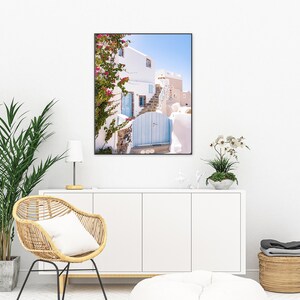 Puede incluir: Un edificio blanco con una puerta azul y flores rosas que crecen en el lateral. El edificio est&aacute; en un lugar soleado con un cielo azul de fondo.