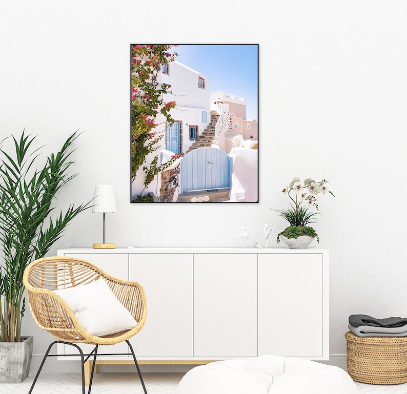 Puede incluir: Un edificio blanco con una puerta azul y flores rosas que crecen en el lateral. El edificio est&aacute; en un lugar soleado con un cielo azul de fondo.