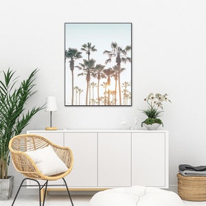 May include: A framed print of a row of palm trees silhouetted against a sunset sky. The print is hanging on a white wall above a white cabinet.