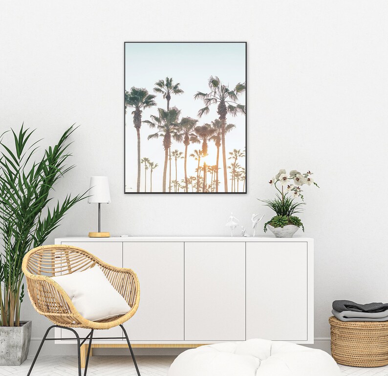 May include: A framed print of a row of palm trees silhouetted against a sunset sky. The print is hanging on a white wall above a white cabinet.