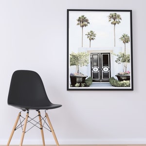 May include: A black and white photo of a double door entrance with palm trees and potted plants. The doors have a white circle design with a black center.