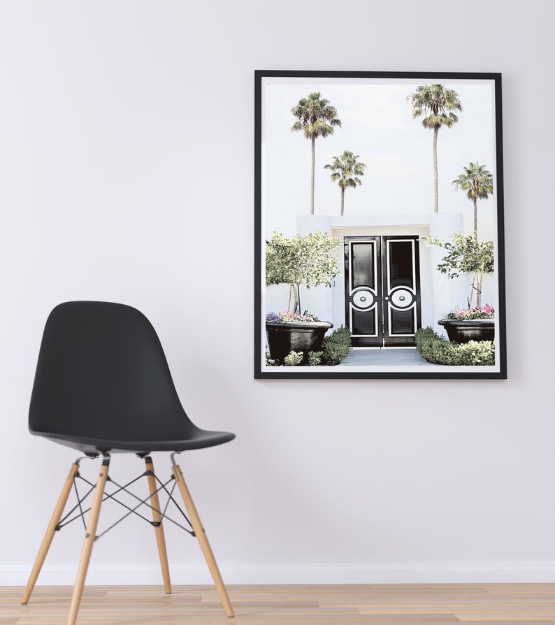 May include: A black and white photo of a double door entrance with palm trees and potted plants. The doors have a white circle design with a black center.