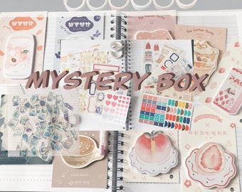 May include: A collection of stationery items, including stickers, sticky notes, and washi tape, arranged on a spiral notebook. The items feature pastel colors and illustrations of peaches, strawberries, and coffee. The text "MYSTERY BOX" is displayed prominently.