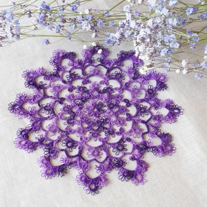 Könnte beinhalten: Eine violette und weiße Häkeldeckchen mit einem zarten, filigranen Design. Die Deckchen ist mit einem Farbverlauf in Violetttönen gearbeitet, wodurch ein wunderschöner Ombre-Effekt entsteht.