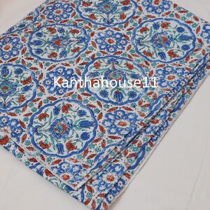 May include: A white cotton fabric with a blue and orange floral pattern. The fabric is folded in thirds and has a white background with a repeating pattern of blue and orange flowers.