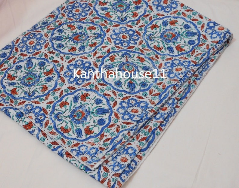 May include: A white cotton fabric with a blue and orange floral pattern. The fabric is folded in thirds and has a white background with a repeating pattern of blue and orange flowers.